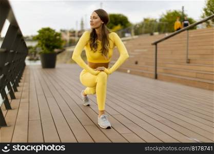 Pretty young woman having stretching exercise on the riverside pier