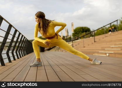 Pretty young woman having stretching exercise on the riverside pier