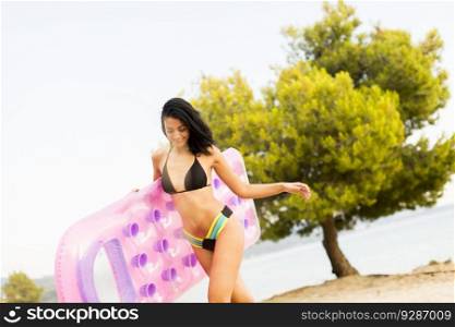 Pretty young woman holding an air mattress on the beach at summer