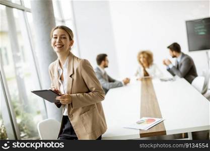Pretty young woman holding digital tablet in modern office in front of her team
