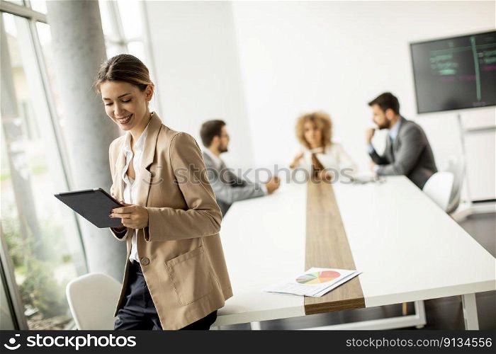 Pretty young woman holding digital tablet in modern office in front of her team