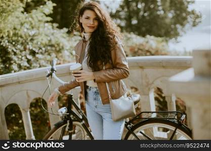 Pretty young woman holding takeaway coffee cup by the bicycle on autumn day