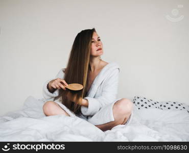 Pretty, young woman in a soft, terry dressing bathrobe, combing her hair after Spa Services and Spa Treatments. Pretty woman combing her hair after Spa