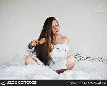 Pretty, young woman in a soft, terry dressing bathrobe, combing her hair after Spa Services and Spa Treatments. Pretty woman combing her hair after Spa