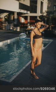 Pretty young woman in bikini posing by the pool  at hot summer day