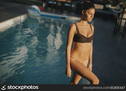 Pretty young woman in bikini posing by the pool  at hot summer day