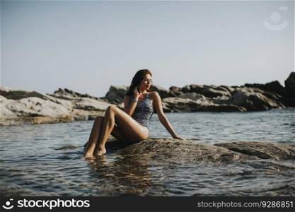Pretty young woman in bikini sitting on rock by the sea