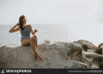Pretty young woman in bikini sitting on rocks by the sea
