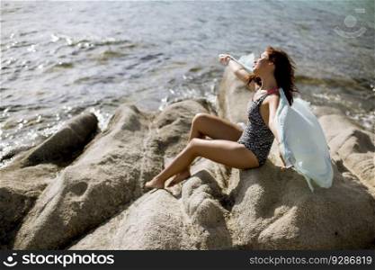 Pretty young woman in bikini sitting on rocks by the sea