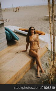 Pretty young woman in bikini sitting on the beach at summer day