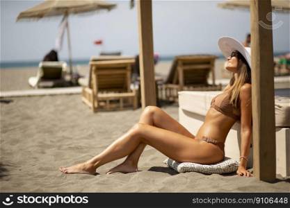 Pretty young woman in bikini sitting on the beach at summer day