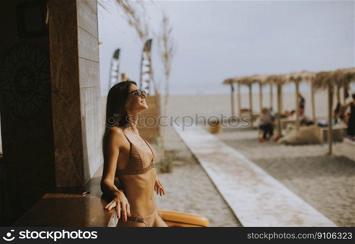 Pretty young woman in bikini standing by the beach bar on a summer day