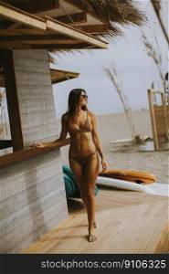 Pretty young woman in bikini standing by the surf cabin on a beach at summer day