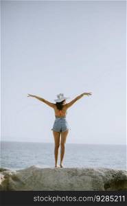 Pretty young woman in bikini standing on rocks by the sea