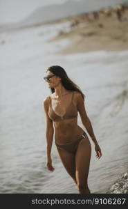 Pretty young woman in bikini walking by the sea on a summer day