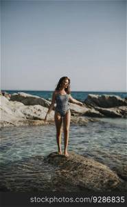 Pretty young woman in bikini walking on rocks by the sea