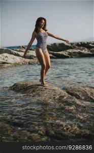 Pretty young woman in bikini walking on rocks by the sea