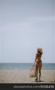 Pretty young woman in bikini with straw bag on the beach at summer day