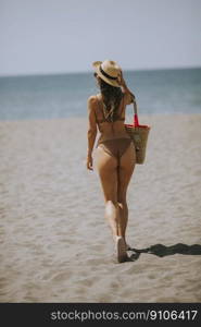 Pretty young woman in bikini with straw bag on the beach at summer day