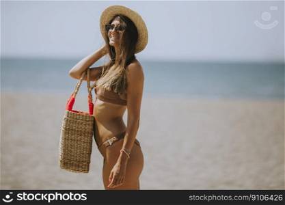 Pretty young woman in bikini with straw bag on the beach at summer day