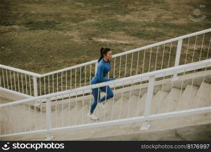 Pretty young woman in blue track suit running on the outdoor stairs at autumn morning