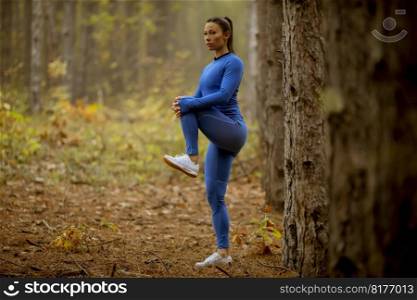 Pretty young woman in blue track suit stretχng before workout in the autumn forest