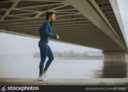 Pretty young woman in blue track suit stretching before workout by the river at autumn morning