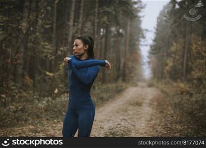 Pretty young woman in blue track suit stretching before workout in the autumn forest