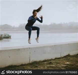 Pretty young woman in blue track suit taking jump by the river at autumn morning