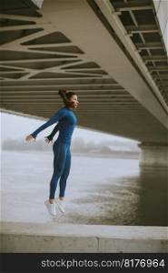 Pretty young woman in blue track suit taking jump by the river at autumn morning