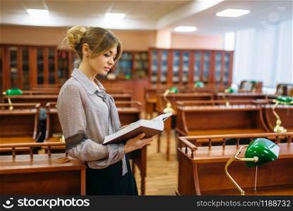 Pretty young woman in reading room, university library. Female person in knowledge depository