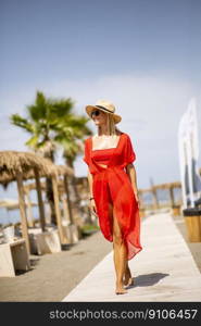 Pretty young woman in red dress walking on a beach at summer