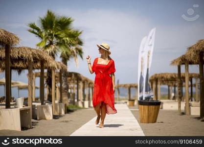 Pretty young woman in red dress walking on a beach at summer