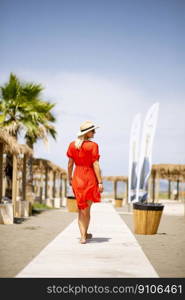 Pretty young woman in red dress walking on a beach at summer