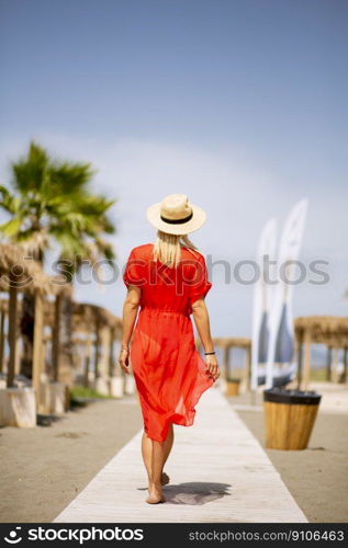 Pretty young woman in red dress walking on a beach at summer