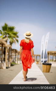 Pretty young woman in red dress walking on a beach at summer