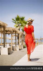 Pretty young woman in red dress walking on a beach at summer