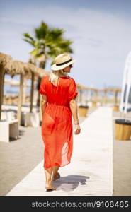 Pretty young woman in red dress walking on a beach at summer