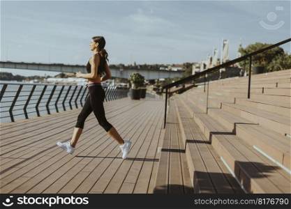 Pretty young woman in sportswear exercising on a river promenade