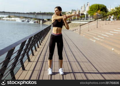 Pretty young woman in sportswear exercising on a river promenade