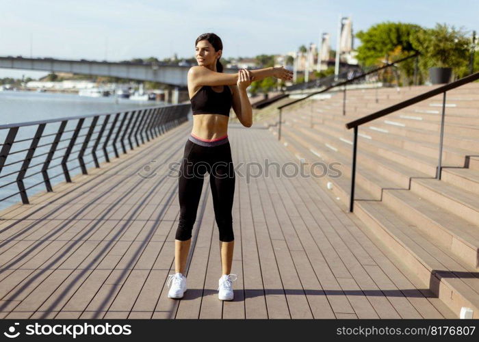 Pretty young woman in sportswear exercising on a river promenade