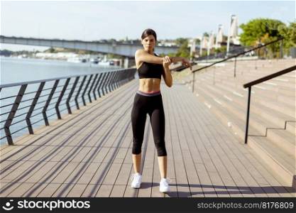 Pretty young woman in sportswear exercising on a river promenade