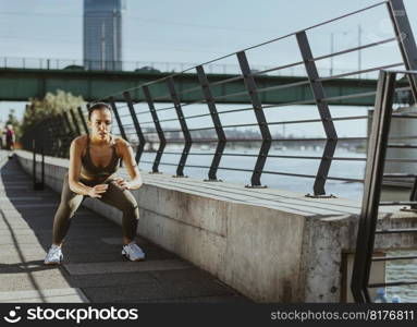 Pretty young woman in sportswear exercising on a river promenade