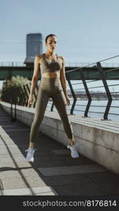 Pretty young woman in sportswear exercising on a river promenade