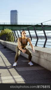 Pretty young woman in sportswear exercising on a river promenade