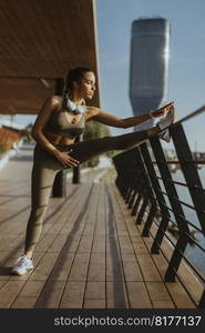 Pretty young woman in sportswear exercising on a river promenade