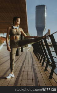 Pretty young woman in sportswear exercising on a river promenade