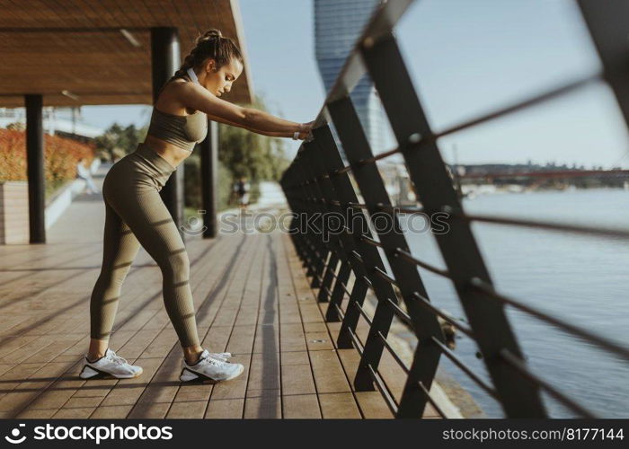 Pretty young woman in sportswear exercising on a river promenade