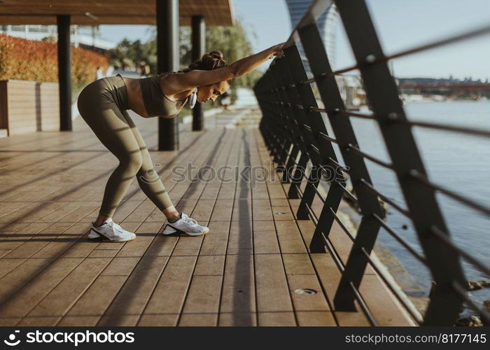 Pretty young woman in sportswear exercising on a river promenade