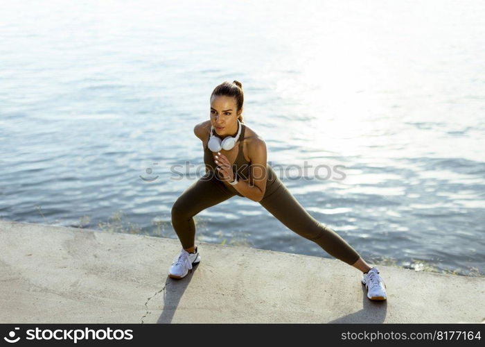 Pretty young woman in sportswear exercising on a river promenade